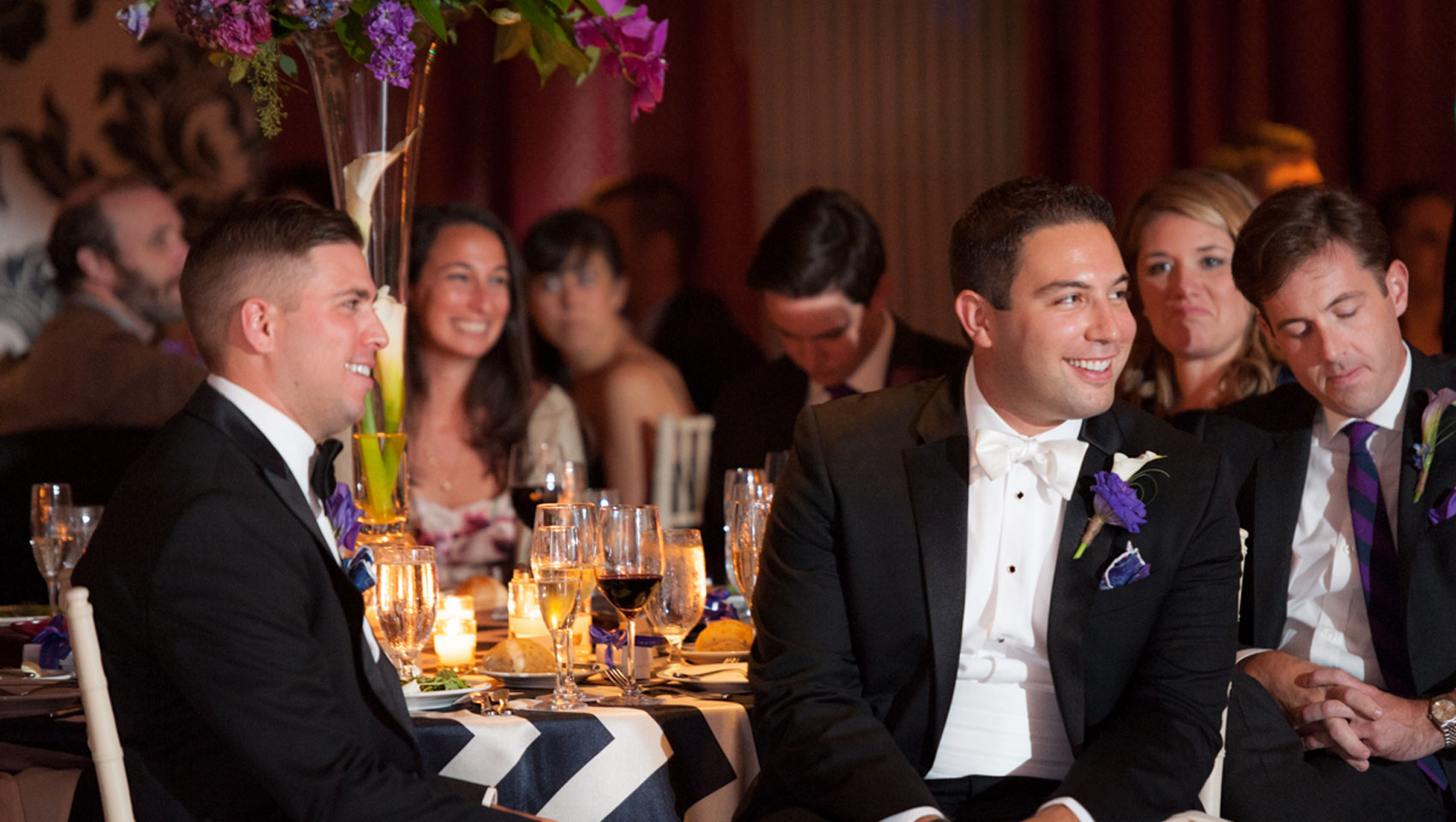 Grooms sit at reception table listening to speeches at Hotel Monaco Baltimore