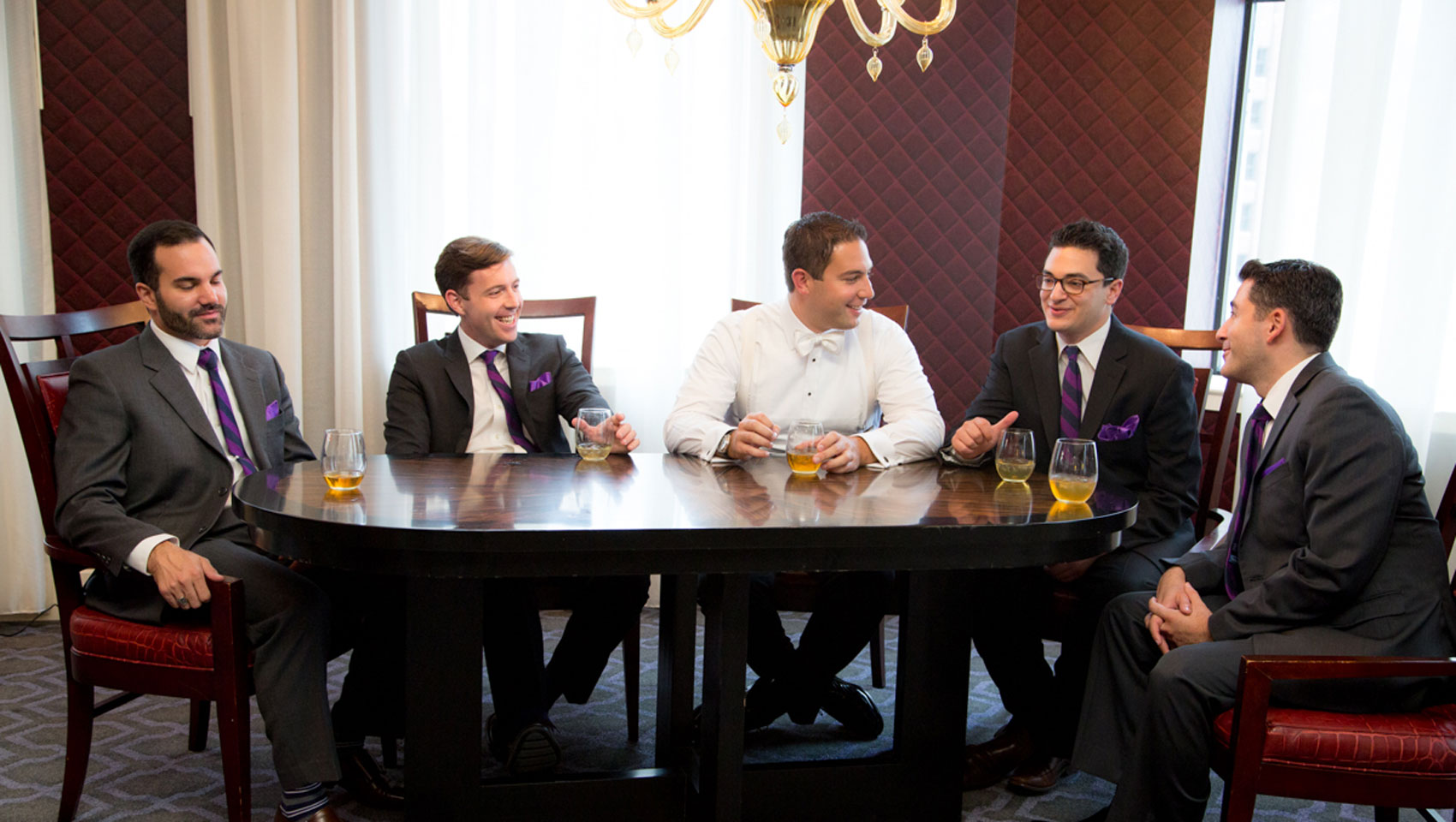 Groom and groomsmen ait at a table each with a cocktail at Hotel Monaco Baltimore