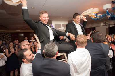 Grooms being lifted on chairs on dance floor